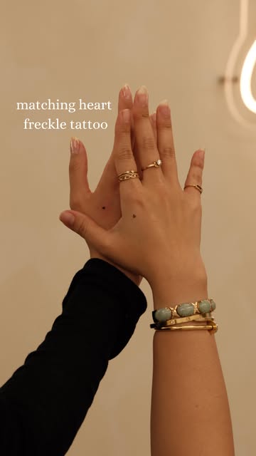 Two hands showing matching tiny heart freckle tattoos