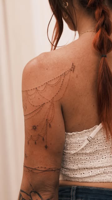 Delicate ornamental fineline tattoo draped across a shoulder and upper arm