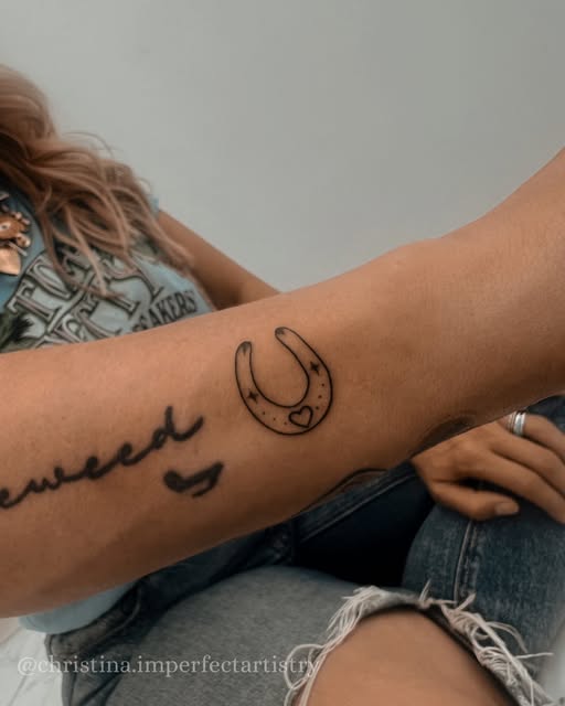 Small outlined horseshoe tattoo with a heart detail on a forearm